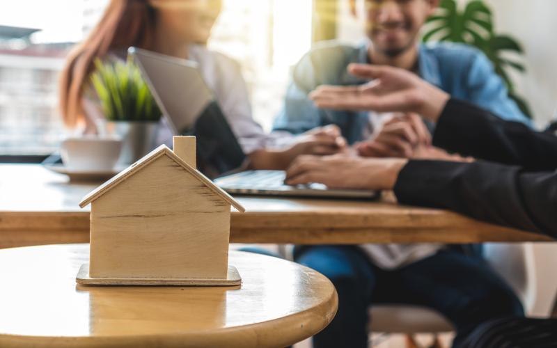 Close up of wooden home model with three people behind speaking