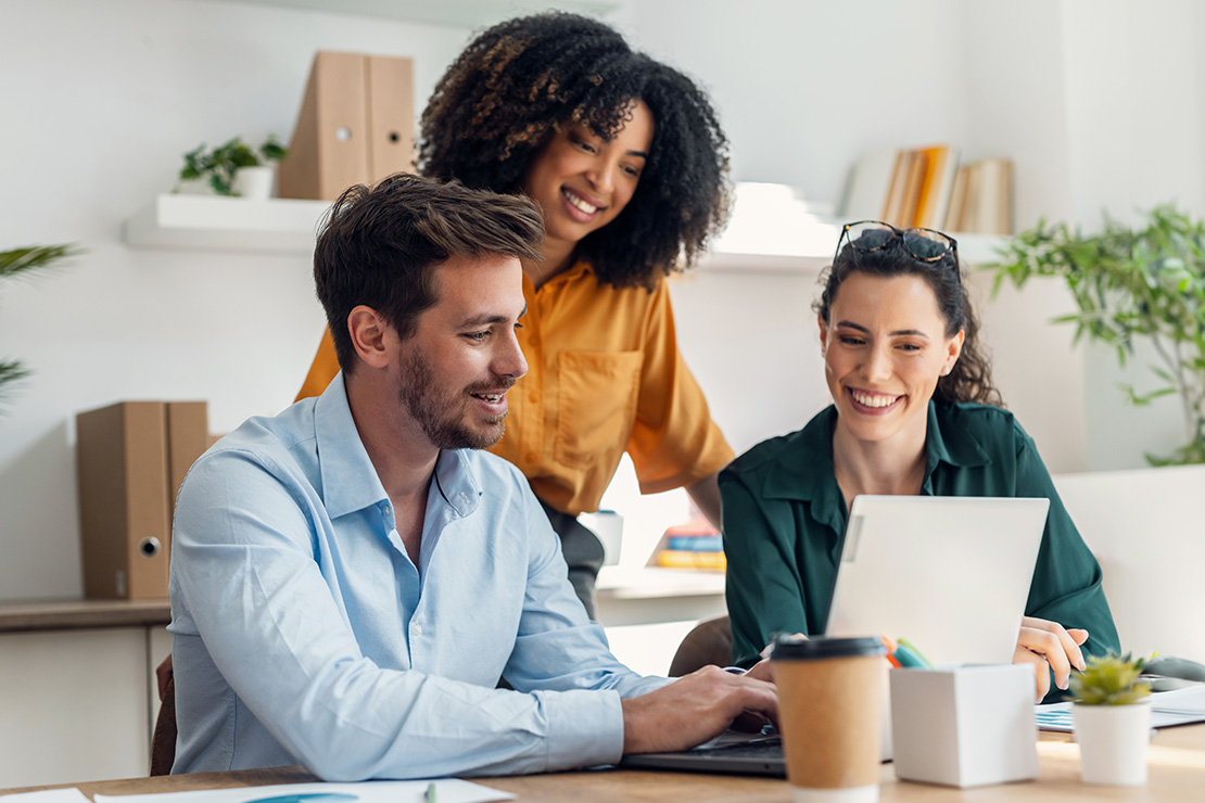 Three people smiling beside a laptop computer