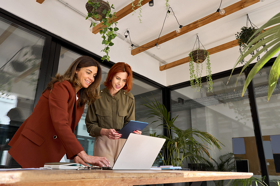 Two females looking at a laptop surrounded by hanging plants