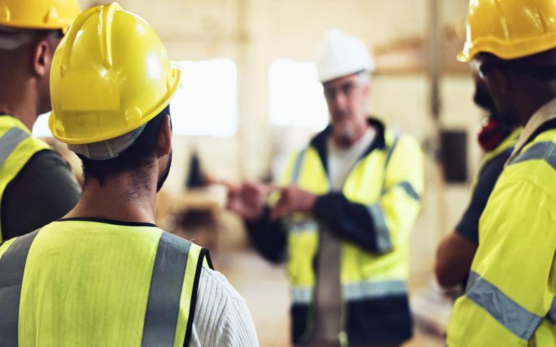 back view of workers in yellow helmets and high-vis vests listening to foreman speaking