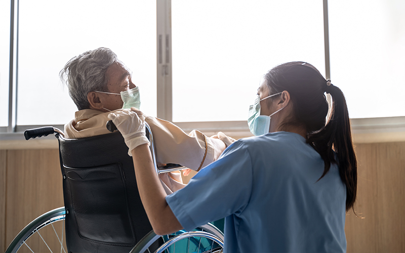 Nurse attends to elderly patient in a face mask