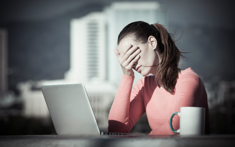 Woman has head in hands at a desk working from home.